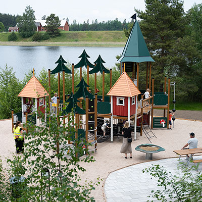 Large playground unit with forest theming, nestled amongst trees next to a large Swedish lake.
